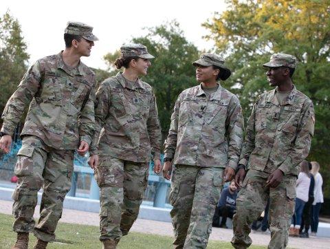 Four students in military uniform chat as they walk on campus.